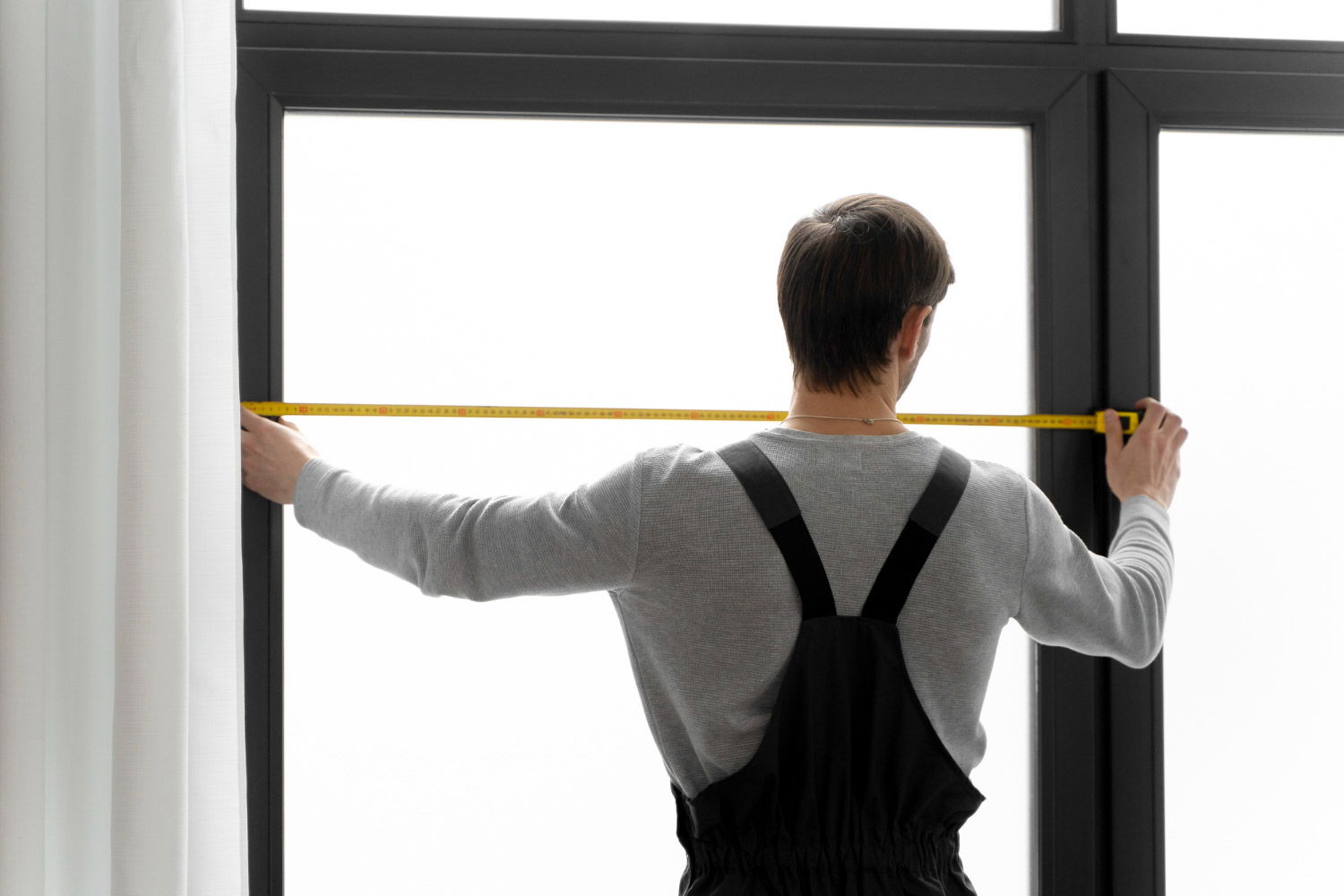 A man holding a measuring tape in front of a window.